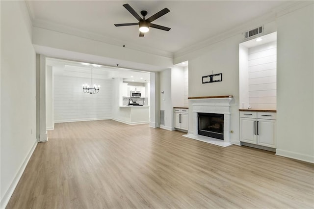 unfurnished living room featuring ceiling fan with notable chandelier, light hardwood / wood-style flooring, and crown molding