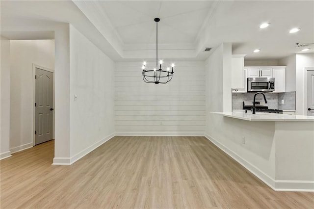 unfurnished dining area with light hardwood / wood-style floors, a raised ceiling, and an inviting chandelier