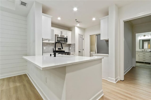 kitchen featuring white cabinets, kitchen peninsula, appliances with stainless steel finishes, and light hardwood / wood-style flooring