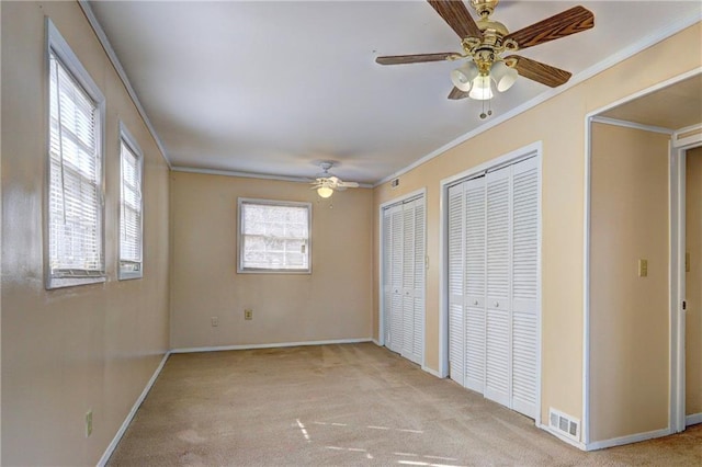 unfurnished bedroom featuring ceiling fan, light colored carpet, ornamental molding, and multiple closets