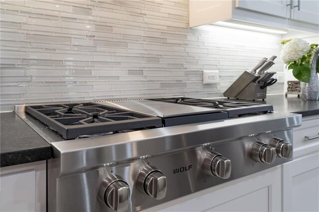 interior details with decorative backsplash, white cabinetry, and range