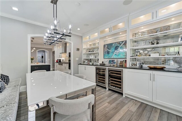 bar with white cabinets, hanging light fixtures, light hardwood / wood-style flooring, ornamental molding, and beverage cooler