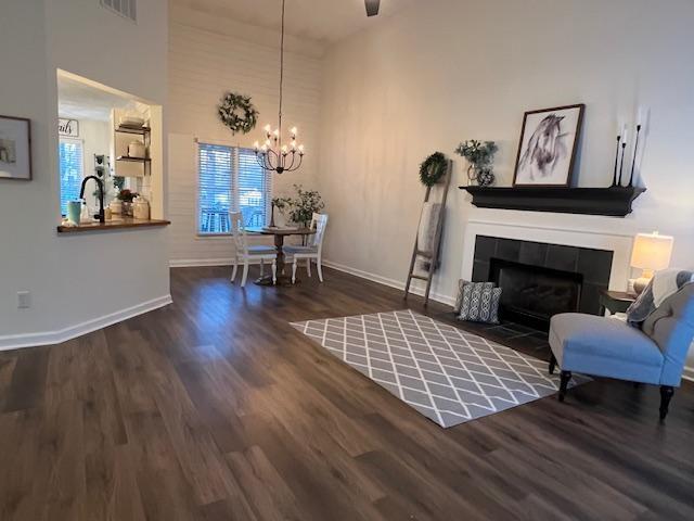 living room with a high ceiling, a fireplace, a chandelier, and dark hardwood / wood-style floors