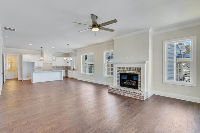 unfurnished living room with ceiling fan with notable chandelier, sink, crown molding, a fireplace, and dark hardwood / wood-style flooring