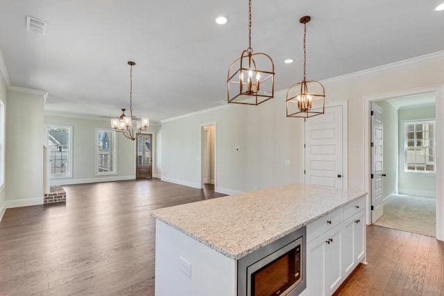 kitchen with hanging light fixtures, white cabinetry, stainless steel microwave, and a kitchen island