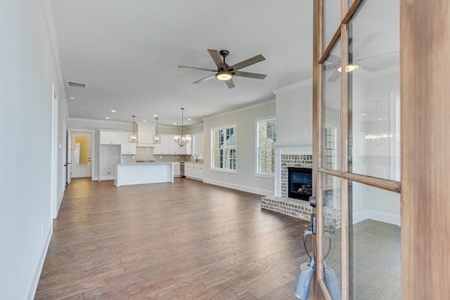 unfurnished living room featuring a fireplace, dark hardwood / wood-style floors, ceiling fan, and crown molding