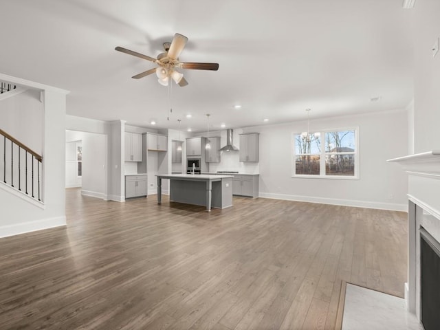 unfurnished living room with crown molding, ceiling fan with notable chandelier, and hardwood / wood-style floors