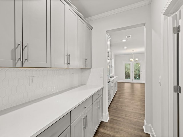 bar with tasteful backsplash, dark wood-type flooring, gray cabinetry, ornamental molding, and a chandelier