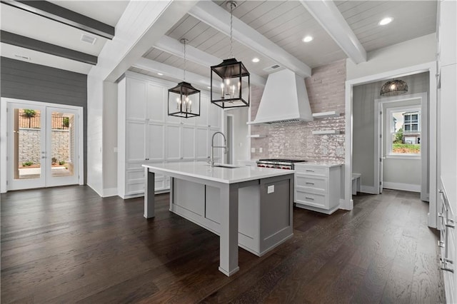 kitchen with tasteful backsplash, dark wood-type flooring, light countertops, custom range hood, and a sink