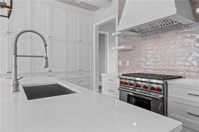 kitchen with tasteful backsplash, high end stainless steel range oven, custom exhaust hood, white cabinets, and a sink