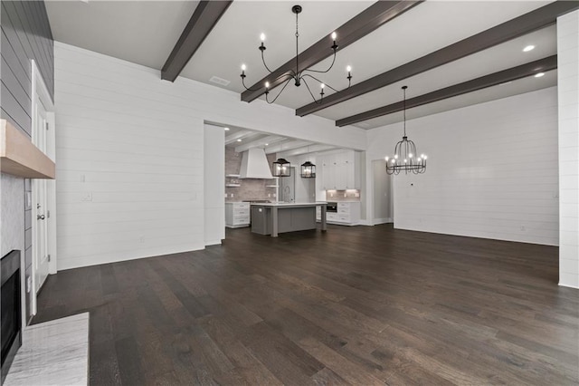 unfurnished living room featuring visible vents, dark wood finished floors, beamed ceiling, a fireplace, and an inviting chandelier