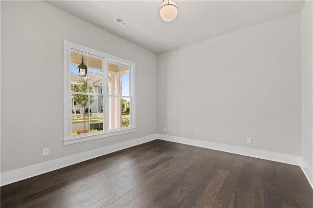 spare room featuring visible vents, dark wood-type flooring, and baseboards