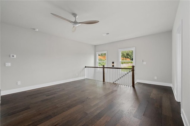 empty room featuring a ceiling fan, dark wood-type flooring, baseboards, and visible vents