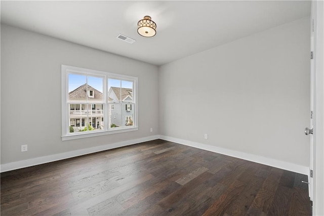 empty room featuring visible vents, baseboards, and dark wood-style floors