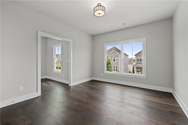 empty room with plenty of natural light, dark wood-style floors, visible vents, and baseboards