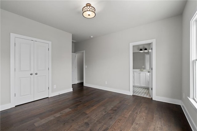 unfurnished bedroom with dark wood finished floors, baseboards, a closet, and ensuite bathroom