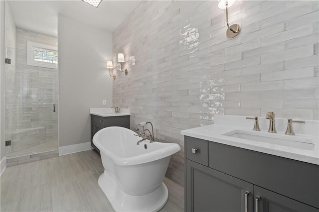 full bath with a freestanding tub, two vanities, a sink, a shower stall, and baseboards