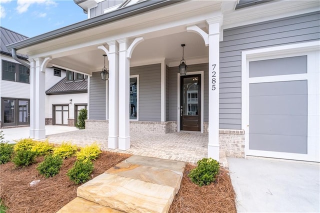 view of exterior entry featuring a standing seam roof, covered porch, a garage, brick siding, and metal roof