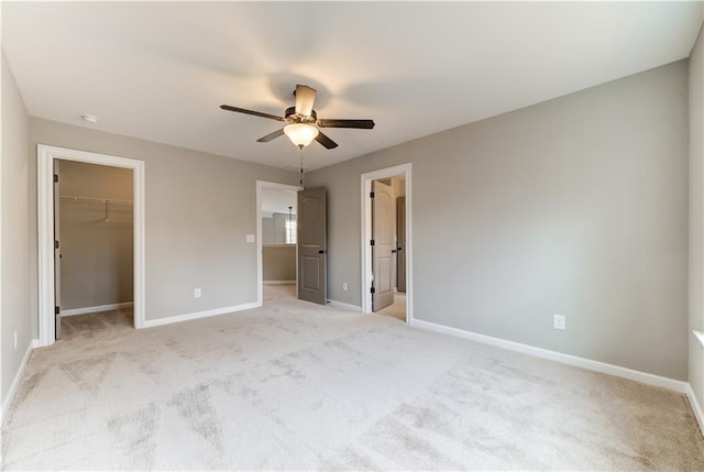 unfurnished bedroom featuring light carpet, a closet, ceiling fan, and a walk in closet