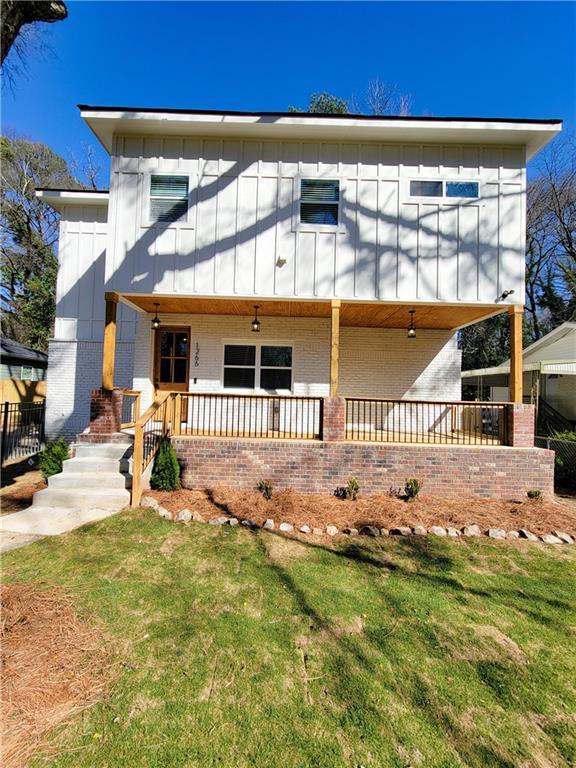 view of front facade with brick siding, board and batten siding, covered porch, and a front yard