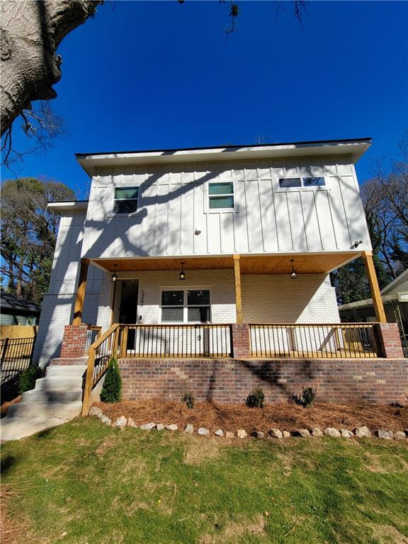 view of front of house with a porch, brick siding, board and batten siding, and a front lawn