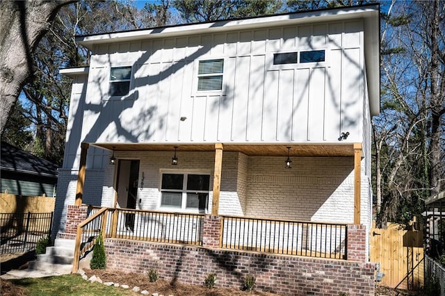 view of front of home featuring a porch, fence, brick siding, and board and batten siding