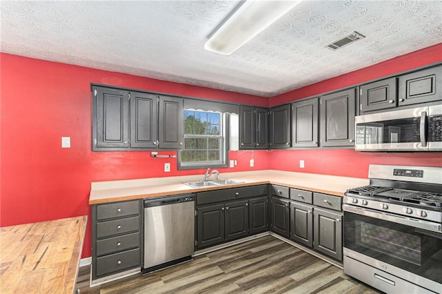 kitchen with dark wood-style flooring, a textured ceiling, visible vents, stainless steel appliances, and a sink