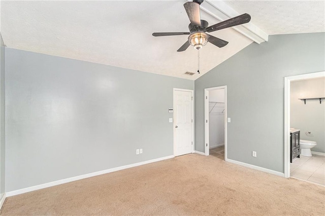 unfurnished bedroom featuring lofted ceiling with beams, a textured ceiling, a walk in closet, connected bathroom, and light carpet