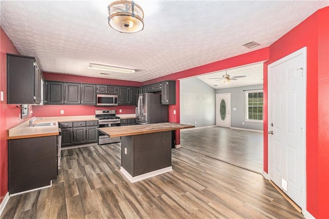 kitchen with a textured ceiling, a ceiling fan, appliances with stainless steel finishes, dark wood-style flooring, and wooden counters
