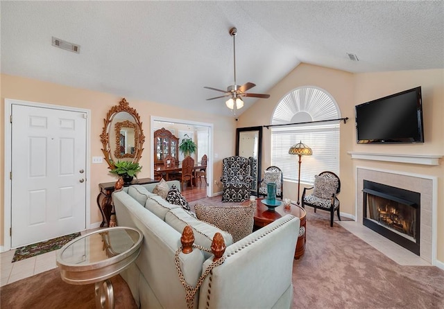 living room with light colored carpet, vaulted ceiling, a textured ceiling, ceiling fan, and a tiled fireplace