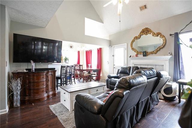 living area featuring ceiling fan, a fireplace, high vaulted ceiling, dark wood finished floors, and visible vents