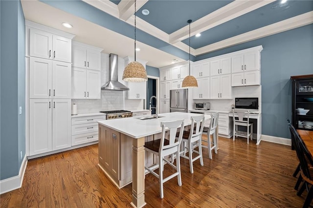 kitchen with an island with sink, high end refrigerator, wall chimney range hood, and white cabinets