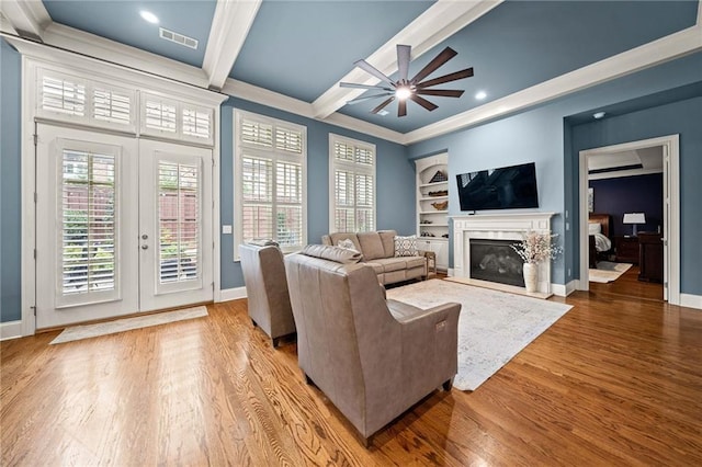 living room featuring hardwood / wood-style flooring, ornamental molding, ceiling fan, beam ceiling, and built in shelves