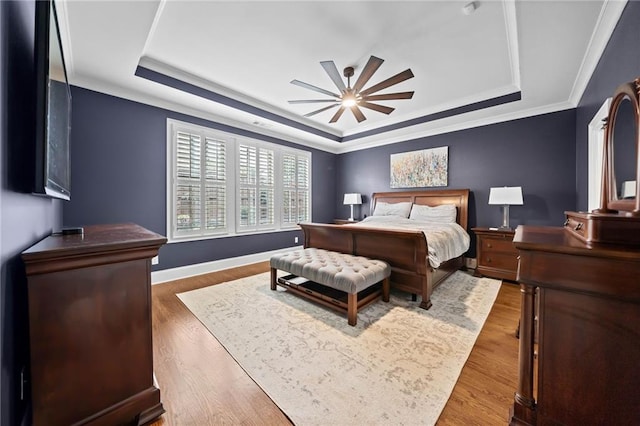 bedroom with crown molding, hardwood / wood-style flooring, a raised ceiling, and ceiling fan