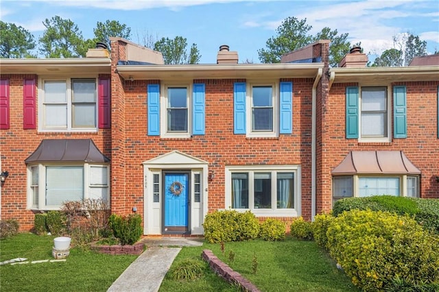 multi unit property featuring a front yard, brick siding, and a chimney