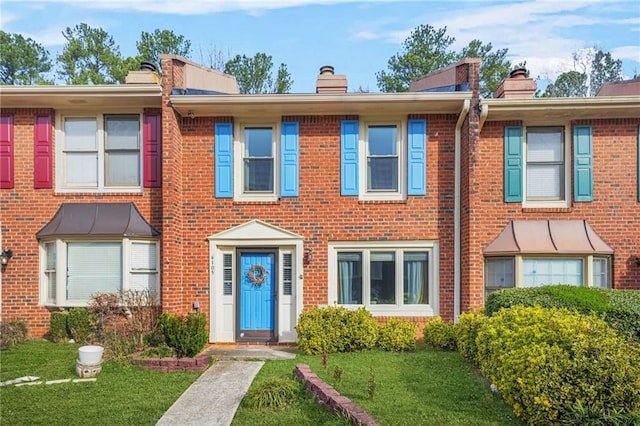 view of property with a front yard, brick siding, and a chimney