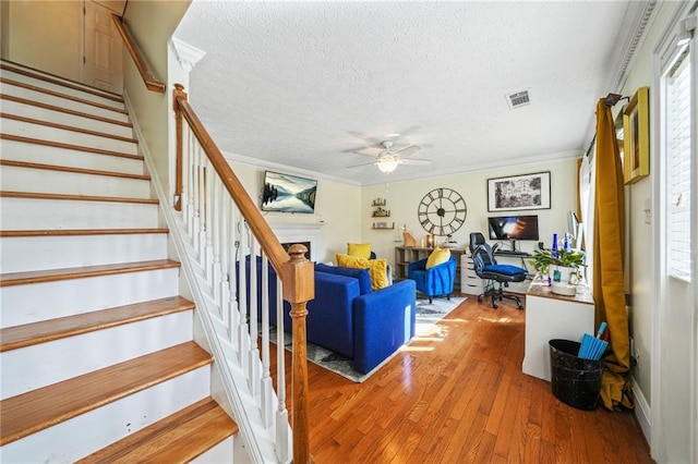 stairs featuring visible vents, ceiling fan, crown molding, and hardwood / wood-style flooring