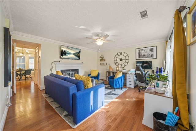 living area featuring visible vents, ornamental molding, ceiling fan, and wood finished floors