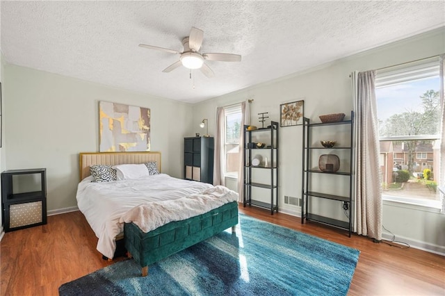 bedroom with visible vents, baseboards, wood finished floors, a textured ceiling, and a ceiling fan