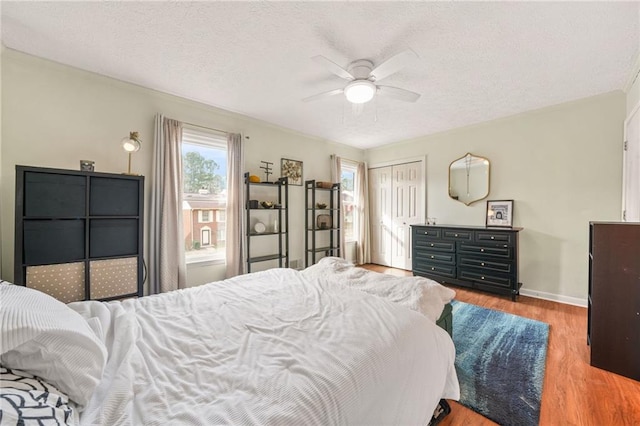 bedroom featuring a ceiling fan, a textured ceiling, wood finished floors, a closet, and baseboards