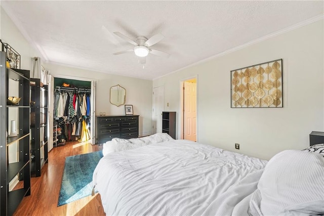 bedroom with a spacious closet, wood finished floors, a closet, and ornamental molding