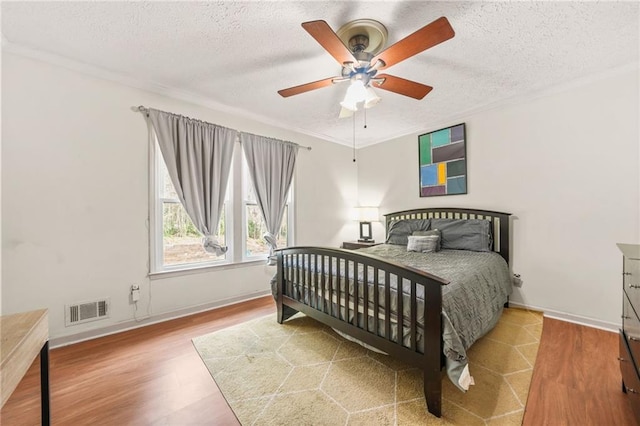 bedroom featuring wood finished floors, baseboards, visible vents, a textured ceiling, and crown molding