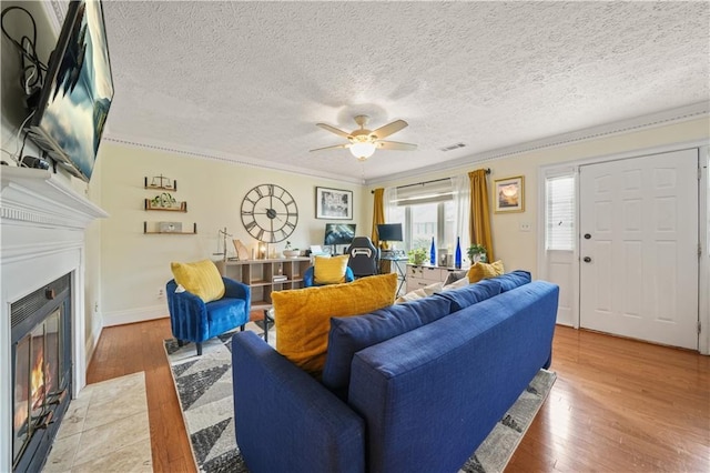 living area with light wood-style flooring, a fireplace with flush hearth, a ceiling fan, and visible vents