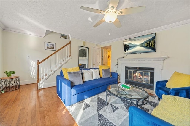 living room featuring stairway, a ceiling fan, hardwood / wood-style flooring, a textured ceiling, and crown molding