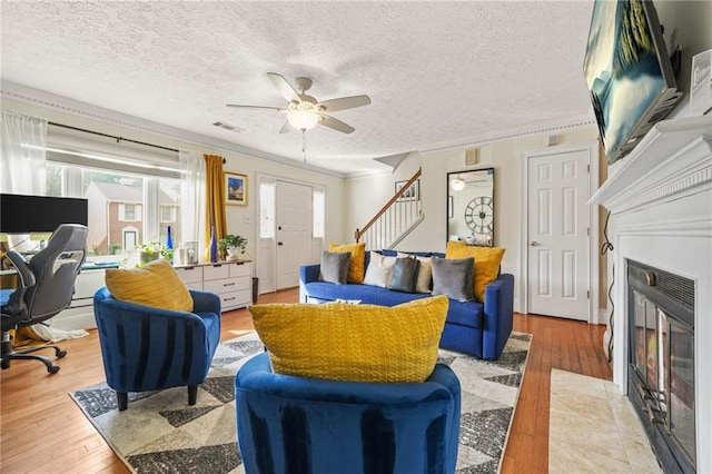 living area with light wood-type flooring, visible vents, a fireplace with flush hearth, a ceiling fan, and stairs