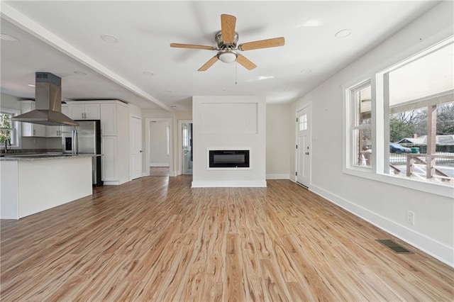 unfurnished living room featuring ceiling fan, sink, and light hardwood / wood-style floors