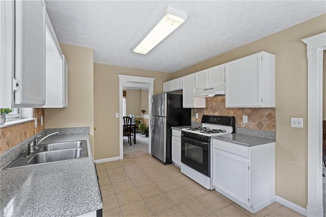 185 Fox Run, Loganville, GA 30052 - kitchen featuring white range with gas stovetop, freestanding refrigerator, under cabinet range hood, tasteful backsplash, and a textured ceiling