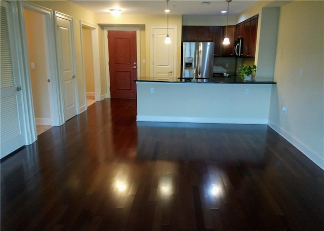 kitchen featuring kitchen peninsula, appliances with stainless steel finishes, dark brown cabinetry, decorative light fixtures, and dark hardwood / wood-style floors