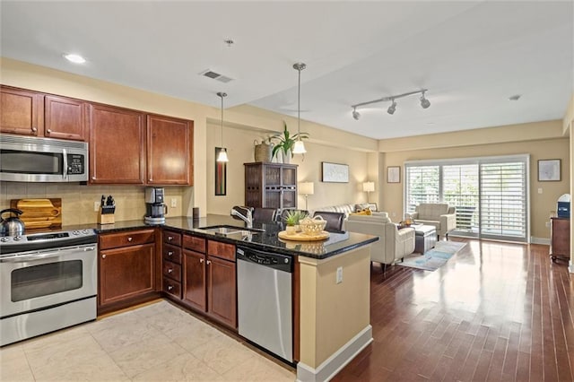 kitchen with kitchen peninsula, light wood-type flooring, stainless steel appliances, sink, and hanging light fixtures