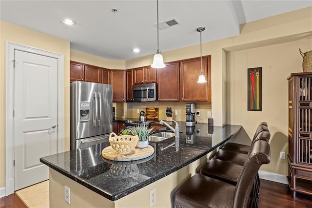 kitchen featuring pendant lighting, hardwood / wood-style flooring, dark stone countertops, appliances with stainless steel finishes, and kitchen peninsula